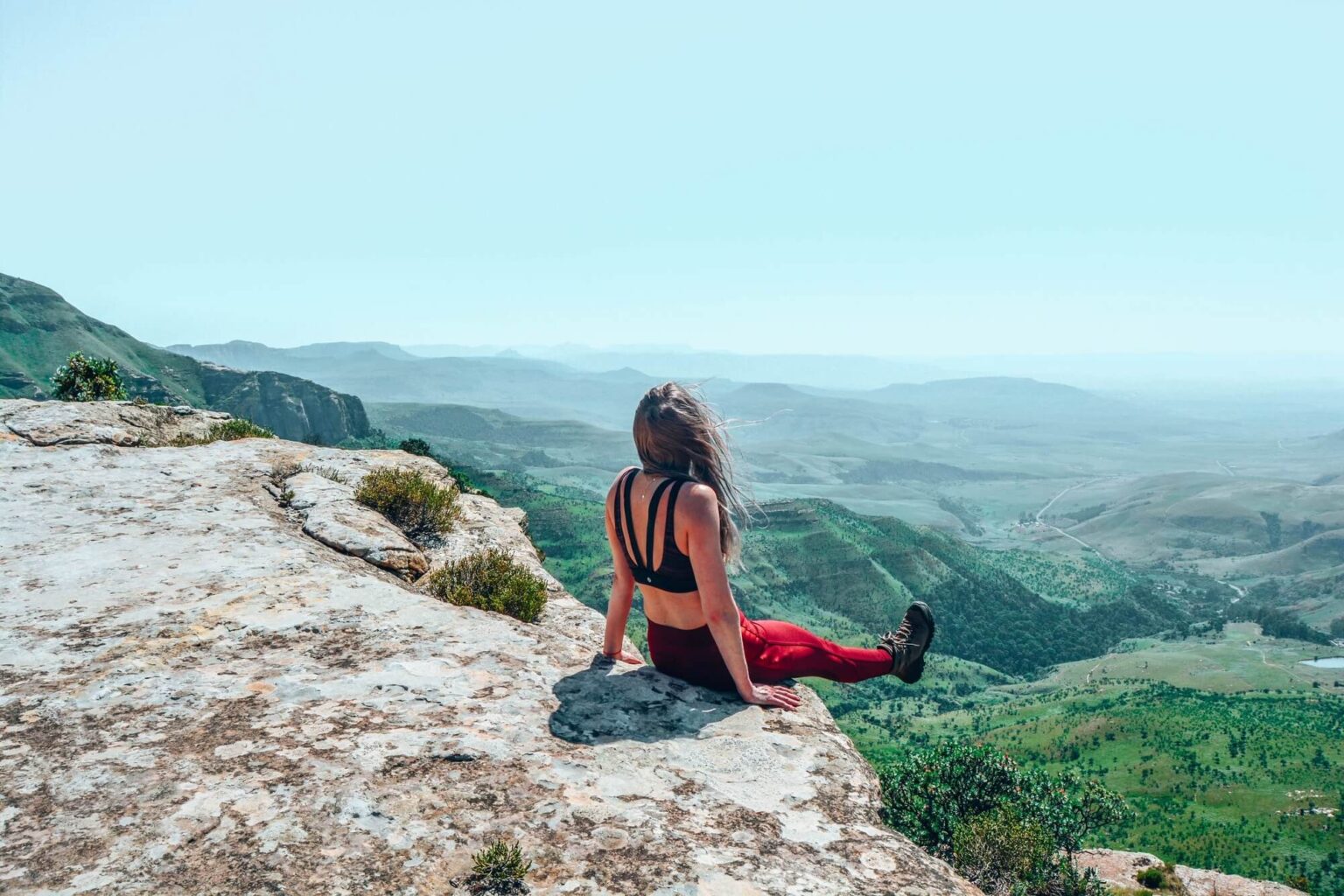 Woman sitting on top of a cliff looking at view of blue horizon