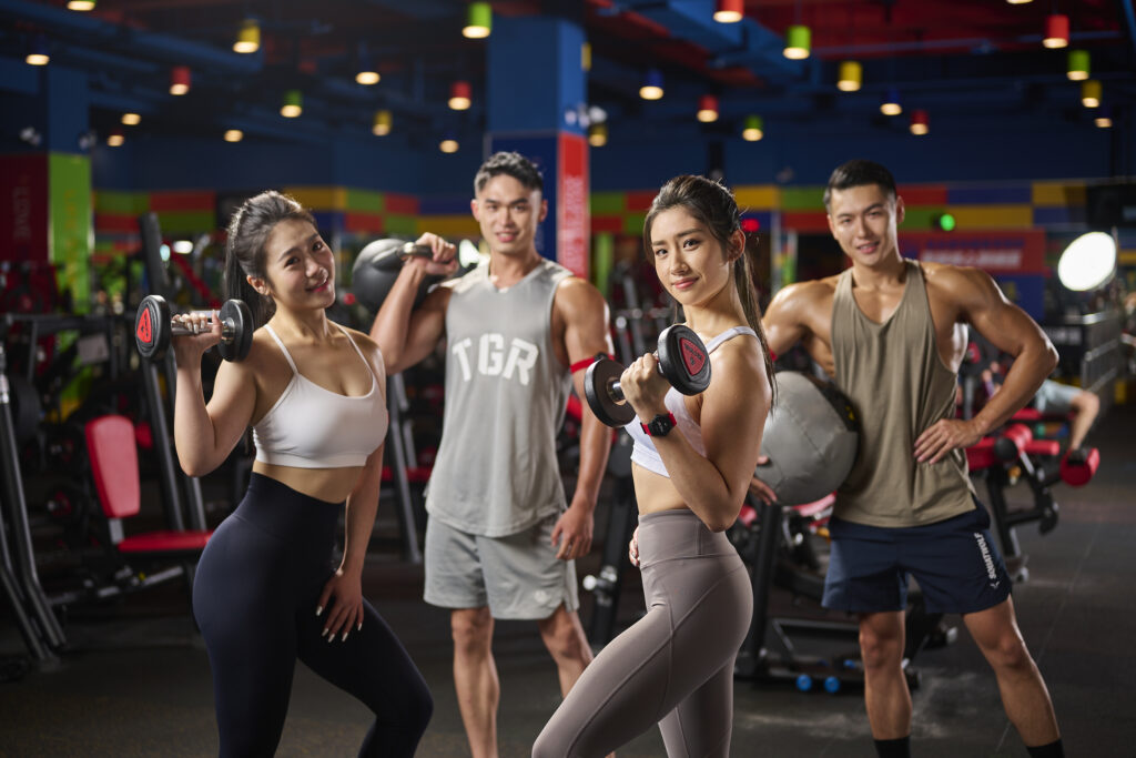 A group of gym members holding various fitness equipment (dumb bells, kettle bells, medicine balls) in the World Gym Taichung Dongshan location.